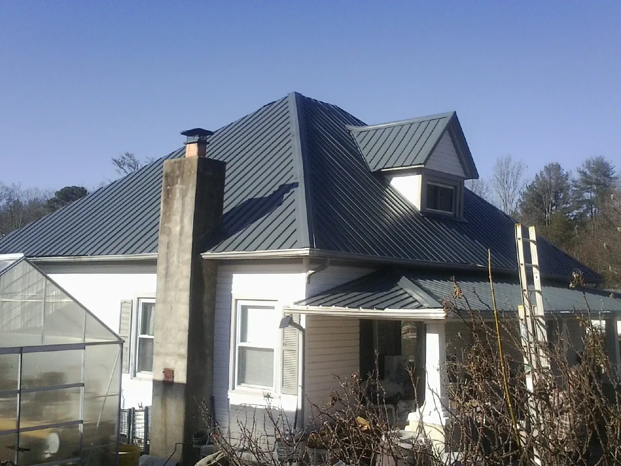 Dark blue standing seam metal roof on a white farmhouse with dormer — Slate & Tile Roof Repair by Roofing Brothers in Arvin