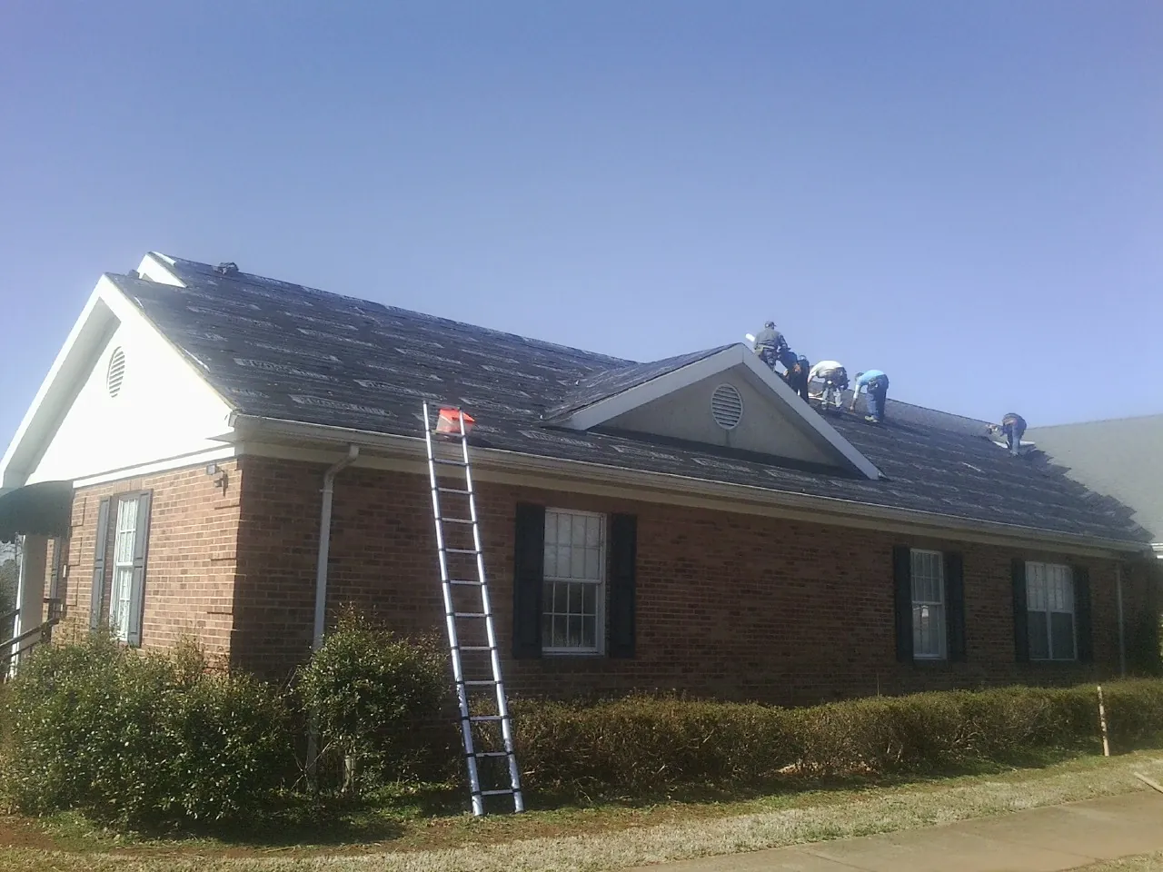 Crew tearing shingles off a brick ranch roof with a ladder set — Emergency Roof Repair work by our crew in Arvin