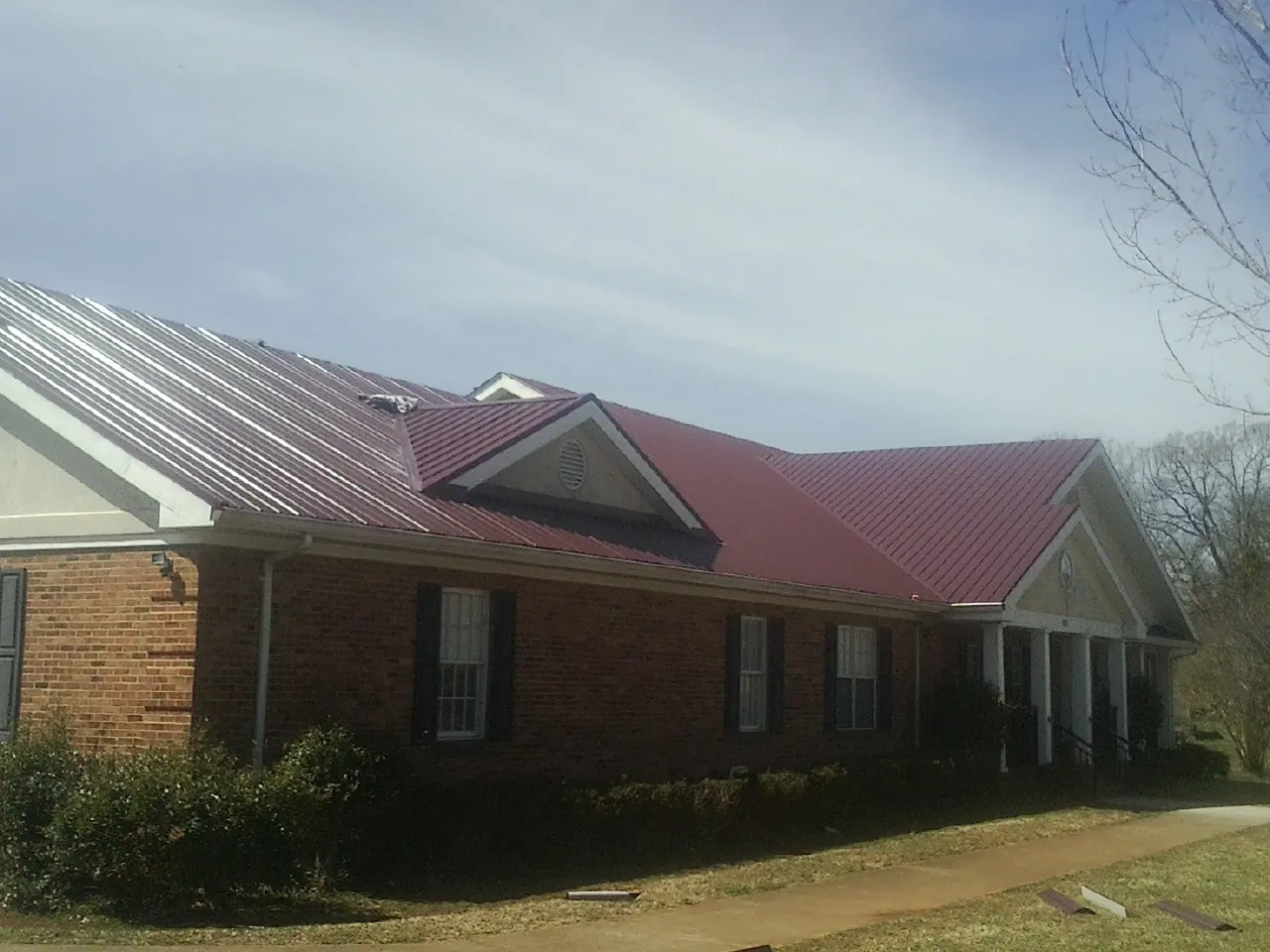 Red metal roof with gabled entries on a long brick building, from a Hail Damage Roof Repair job in Arvin