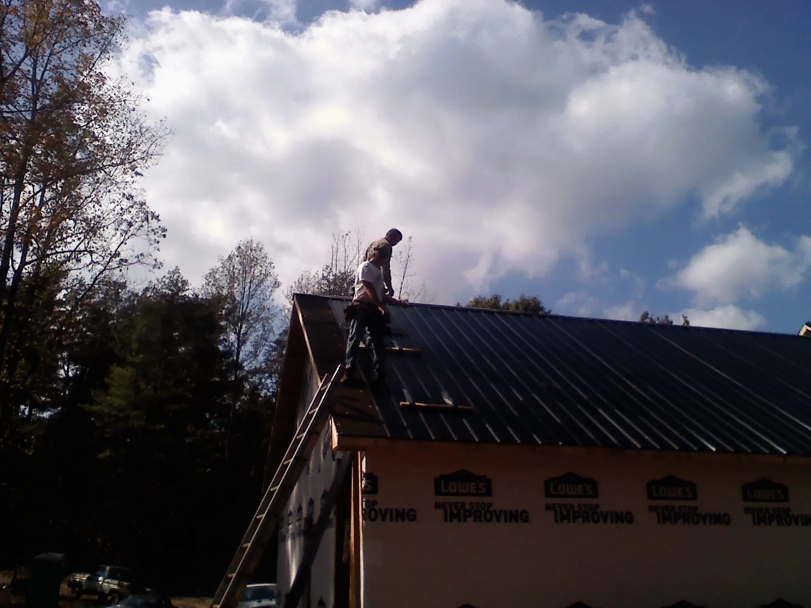 Roofer fastening dark metal panels high against a cloudy sky, from a Roof Inspection job in Arvin