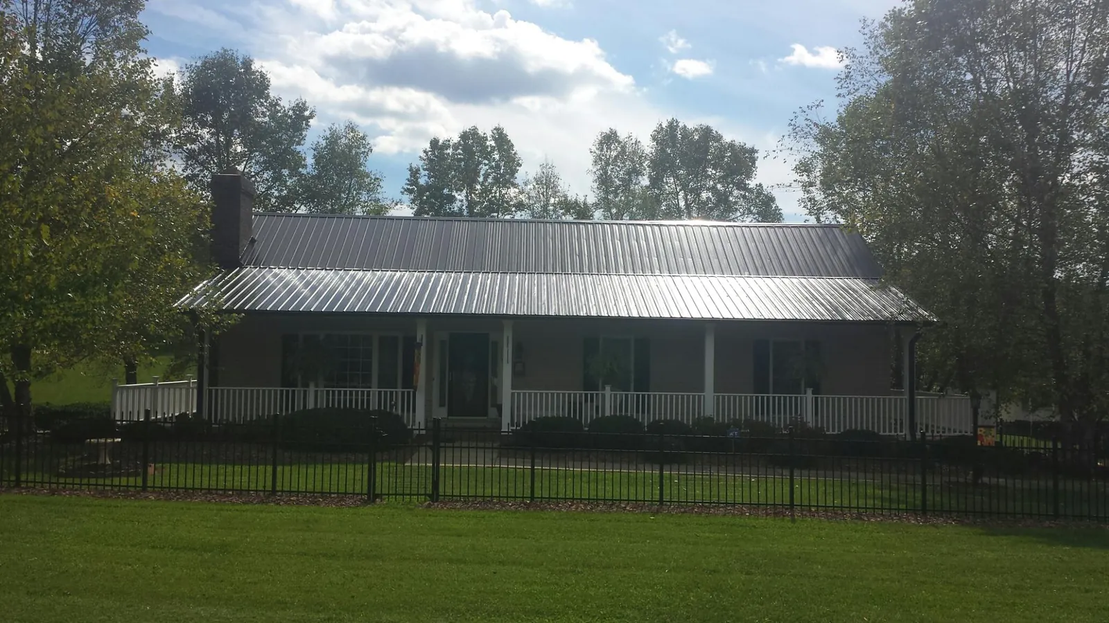 Gray metal roof on a brick ranch with a full width front porch — Gutter Guard Installation work by our crew in Arvin
