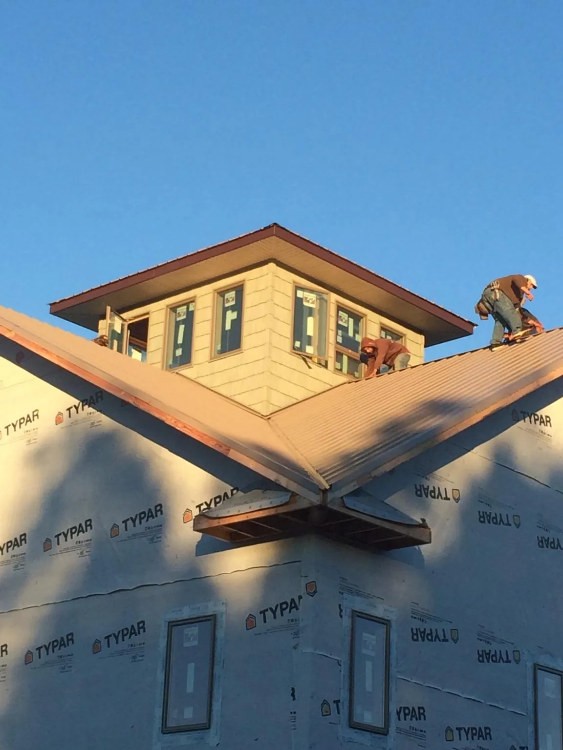 Roofers working around a rooftop cupola on a new metal roof at sunset in Arvin